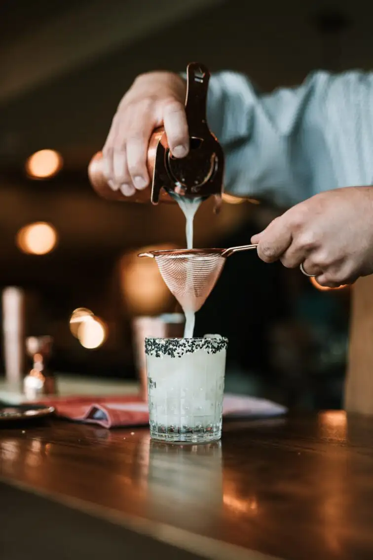 bartender using stainless steel mesh to strain cocktail into glass