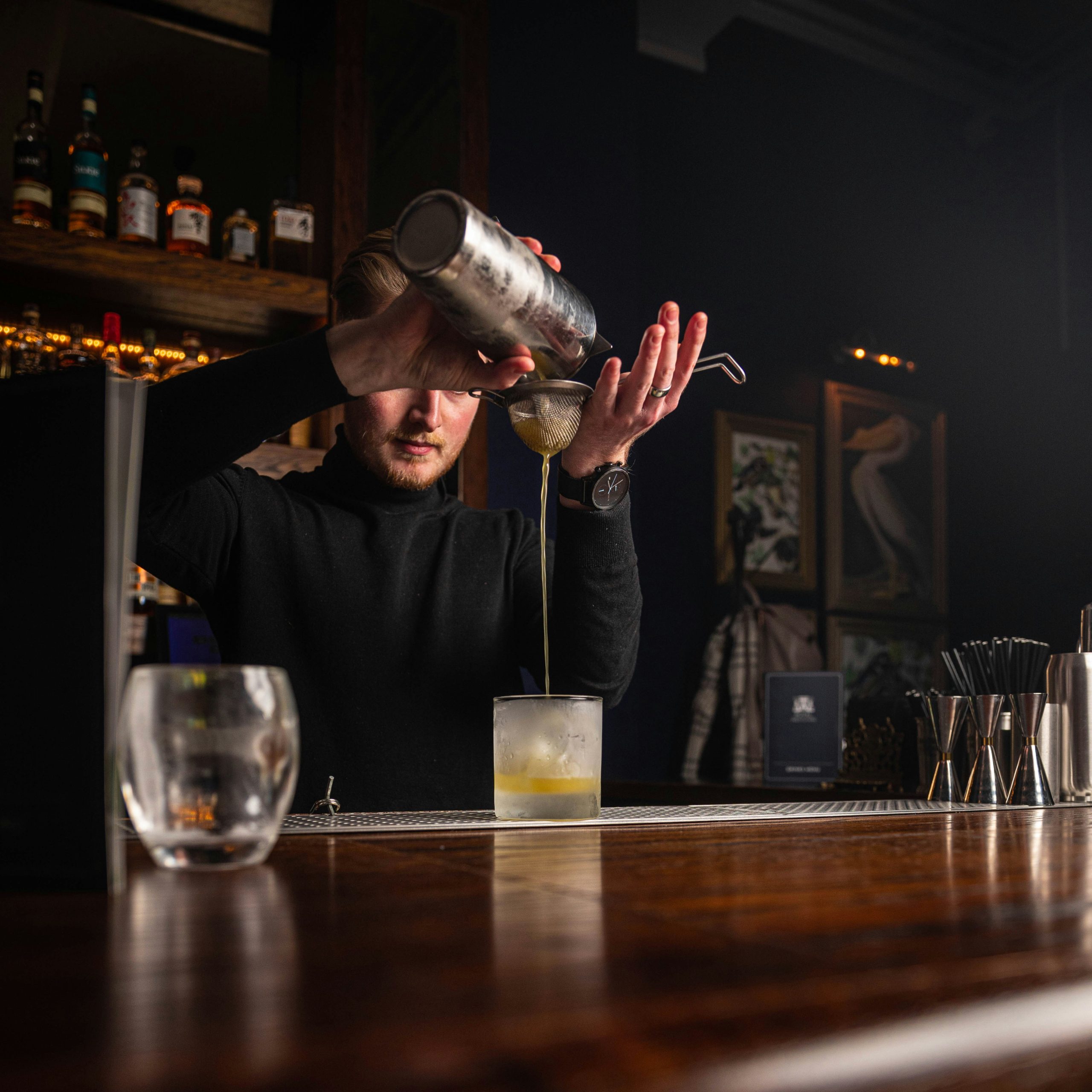 Bartender straining a cocktail through a mesh strainer