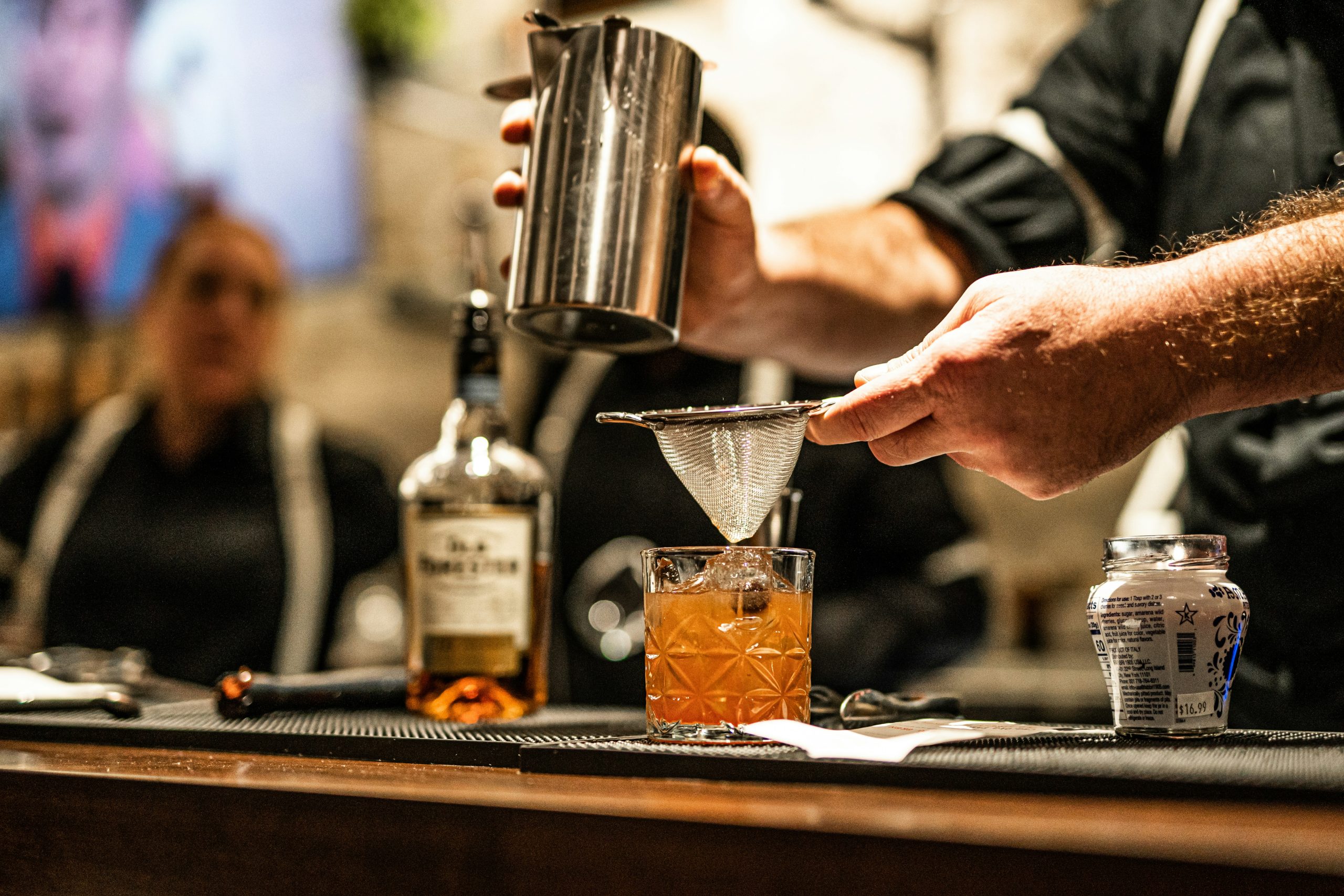 Cocktail being strained with a mesh strainer by a skilled bartender