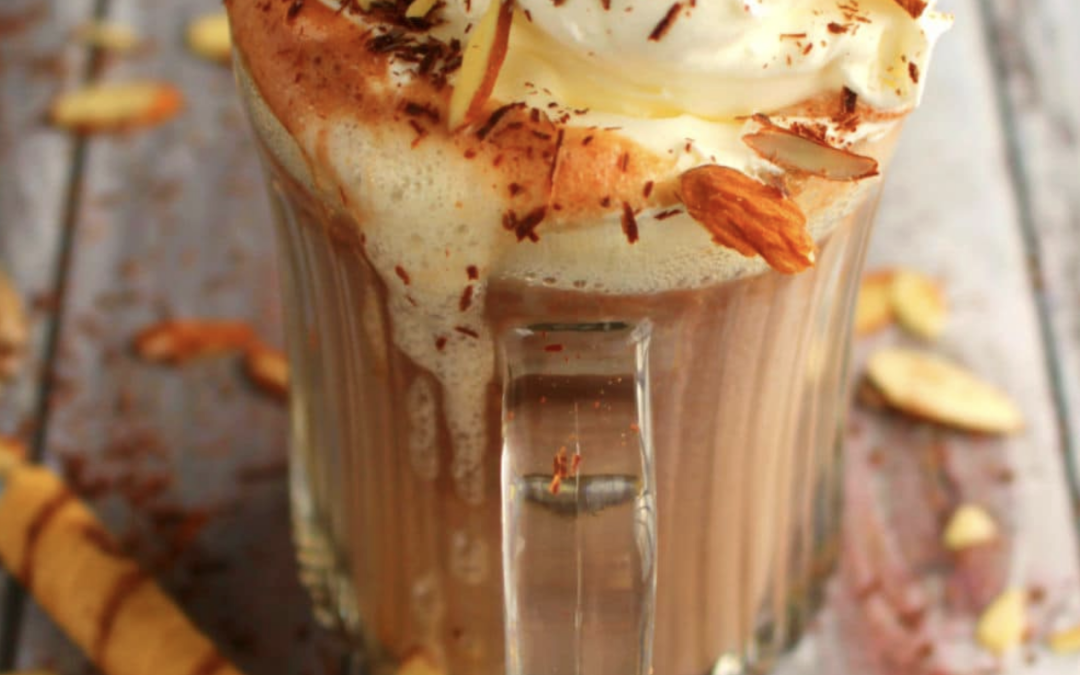 Amaretto Hot Cocoa Cocktail in a clear glass mug, topped with whipped cream and a sprinkle of cocoa powder, almonds, showcasing a rich, chocolatey drink perfect for winter evenings and cozy cocktail recipes.