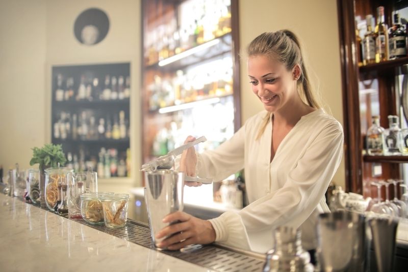 Smiling student practicing cocktail-making techniques with a shaker during bartending training on Long Island.