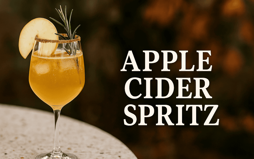 Apple Cider Spritz cocktail in a wine glass with apple slice, rosemary sprig, and cinnamon-sugar rim on a marble table with blurred autumn background