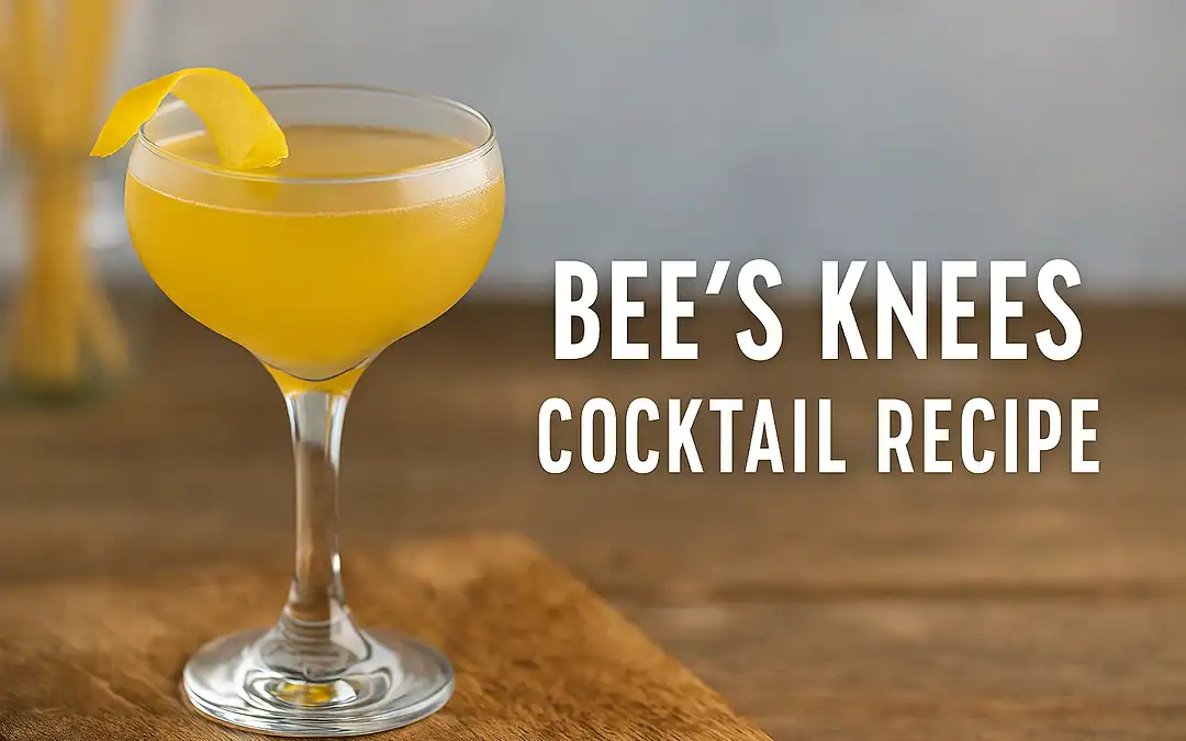 ee’s Knees cocktail in a coupe glass with lemon twist garnish on a wooden bar top, golden honey-colored drink with warm lighting
