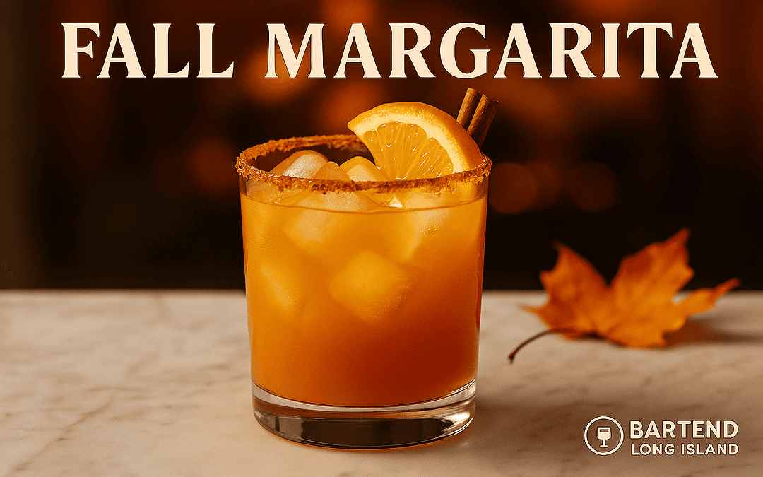 Fall Margarita cocktail recipe in a rocks glass with cinnamon sugar rim, ice, orange wedge, and cinnamon stick garnish. Cozy autumn margarita flavors on a marble bar top with blurred fall leaves in the background.