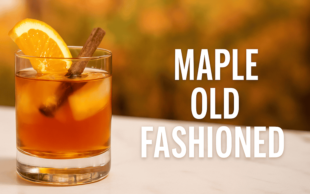 Maple Old Fashioned cocktail in a rocks glass with amber bourbon, large ice cube, orange slice, and cinnamon stick garnish on a marble bar top with blurred autumn background