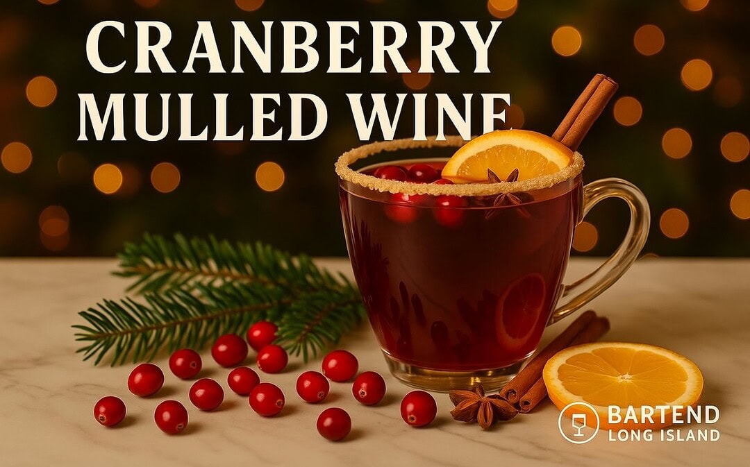 Cranberry Mulled Wine in a glass mug with cinnamon stick, orange slice, cranberries, and star anise, set on a marble surface with pine branches and warm golden Christmas lights in the background with the Bartend Long Island watermark