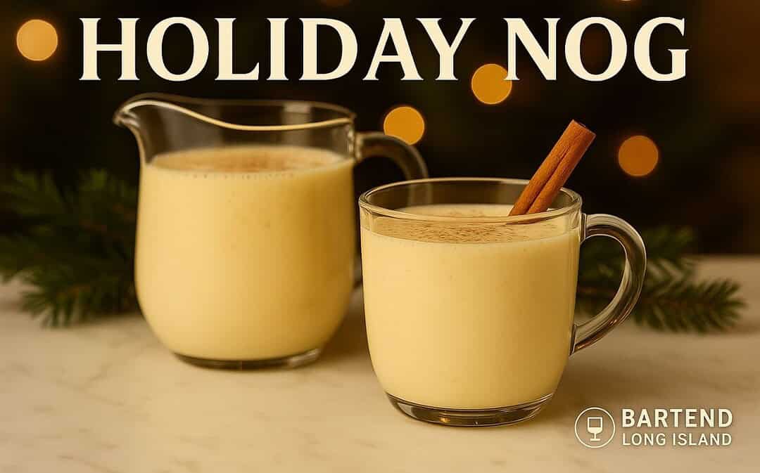 Holiday Nog cocktail in a glass mug with creamy eggnog topped with nutmeg and a cinnamon stick, beside a matching pitcher on marble with pine sprigs and golden Christmas lights in the background.