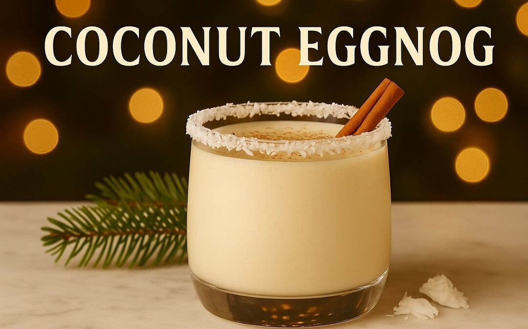 Creamy Coconut Eggnog cocktail in a glass with a coconut-flaked rim and cinnamon stick garnish, set on marble with pine sprigs and warm golden holiday lights in the background.