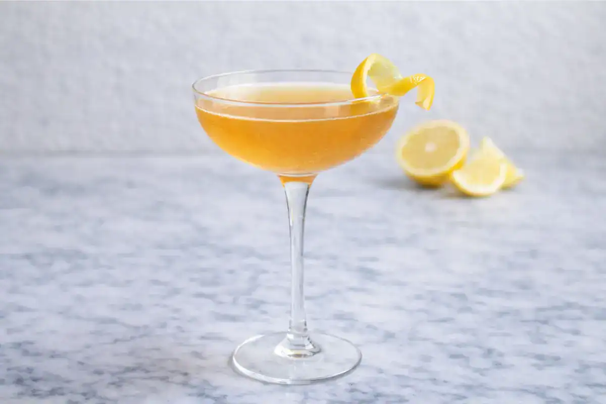 Between the Sheets cocktail in a coupe glass with a light pink tint and a citrus garnish on a bright surface