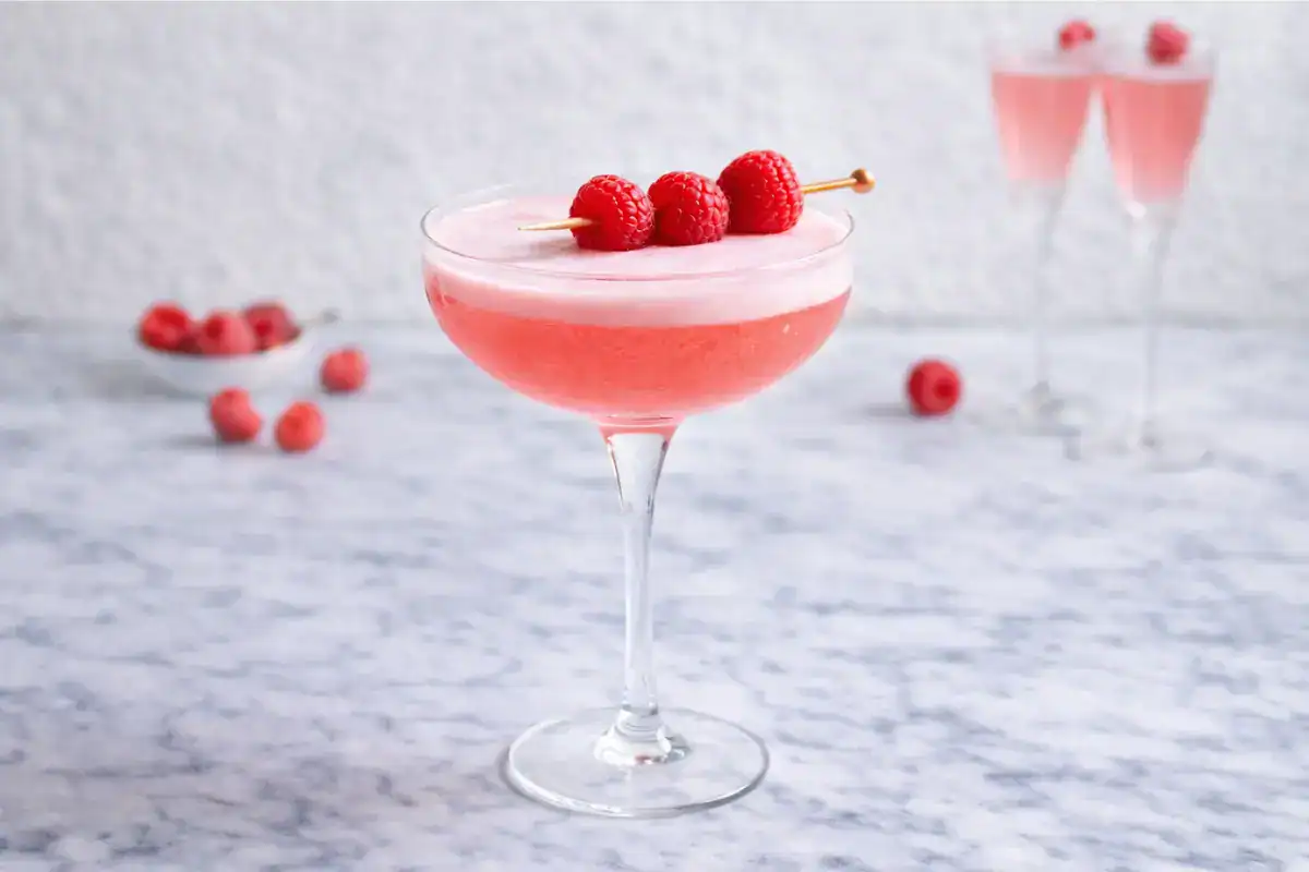 Pink French Kiss cocktail in a coupe glass with a sugared rim and a raspberry garnish