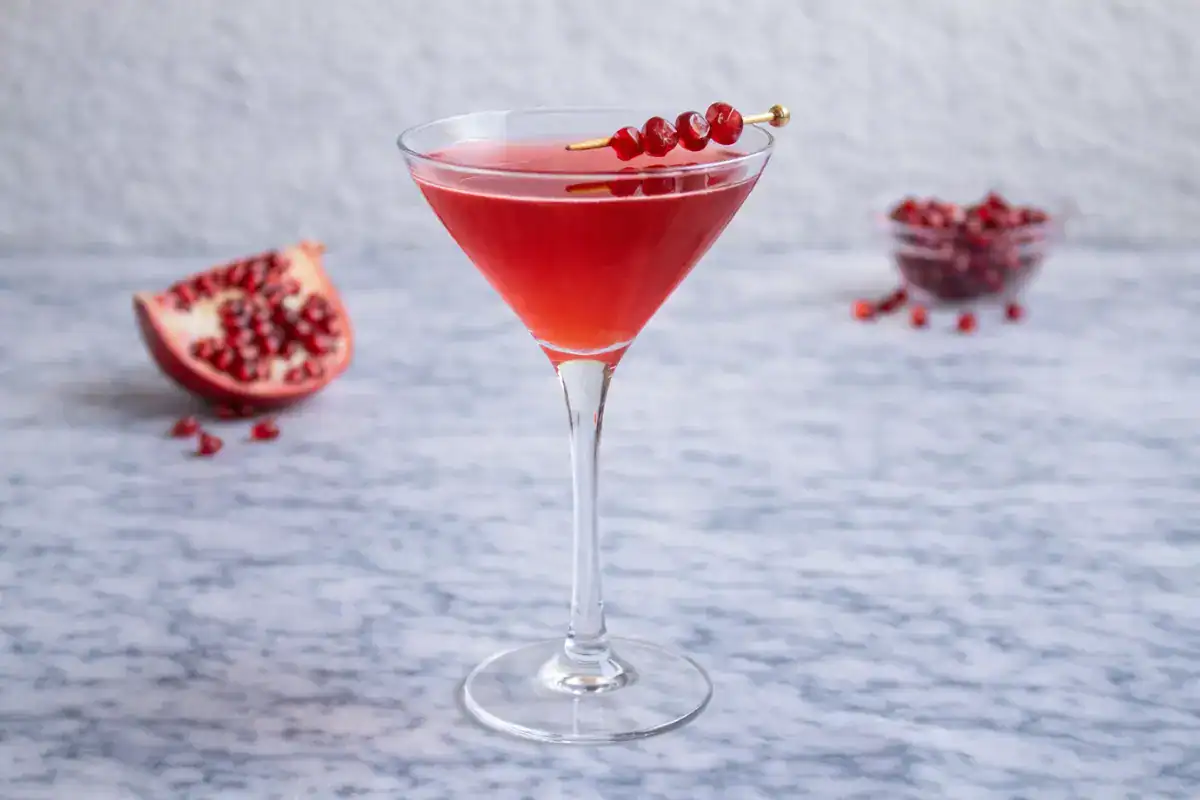 Pomegranate martini in a martini glass with a deep ruby color and pomegranate seeds as garnish