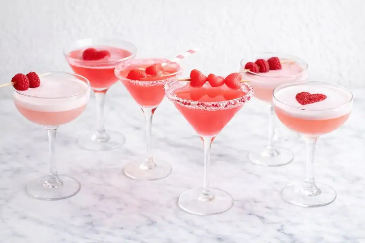 A romantic lineup of Valentine’s Day cocktails in coupe and martini glasses with pink and red garnishes on a bright marble surface