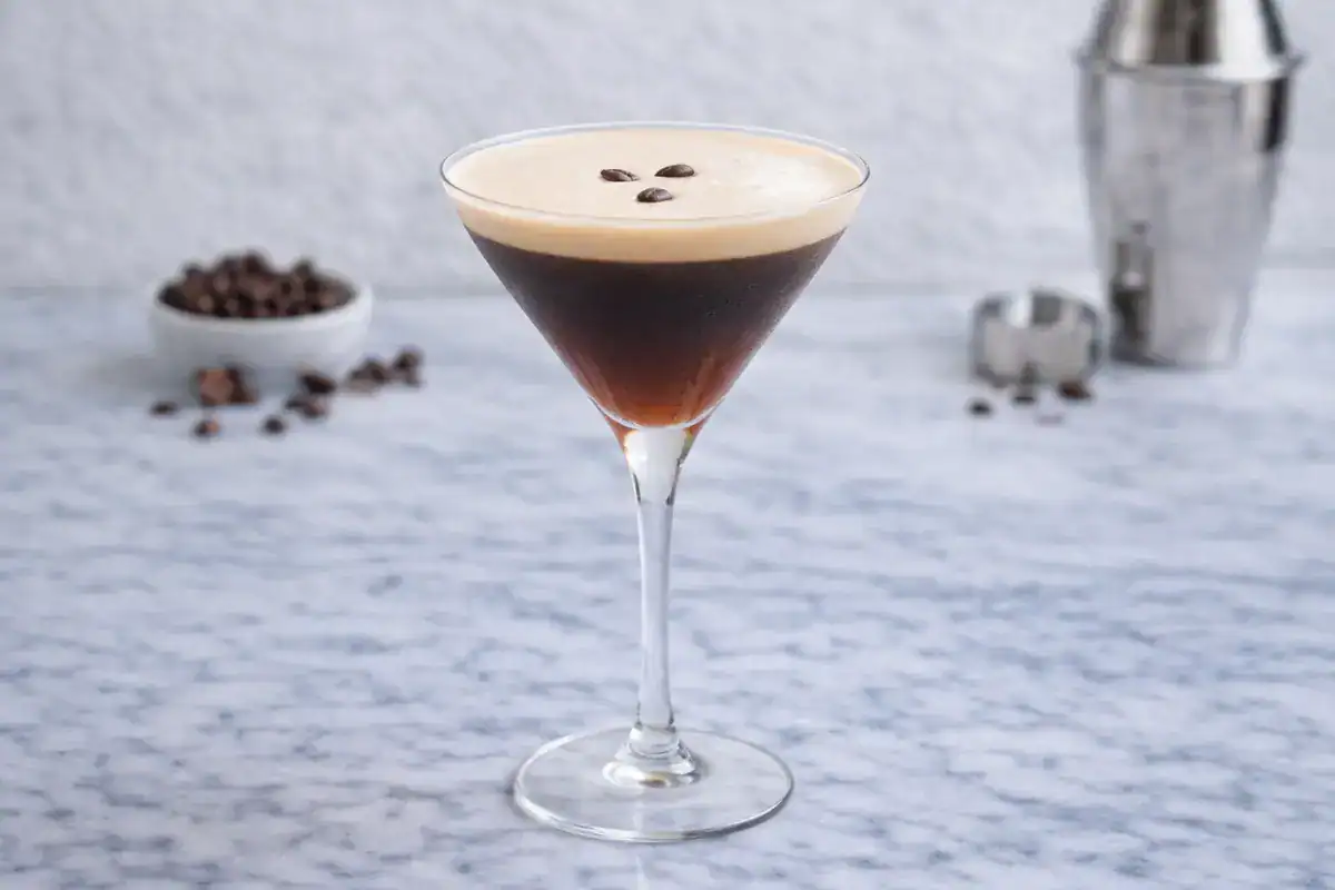 Espresso martini with creamy foam in a coupe glass garnished with coffee beans on a light surface