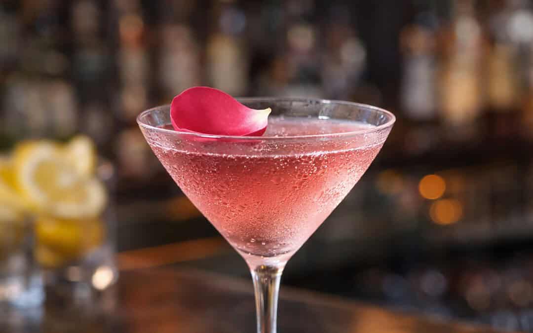 Rose martini cocktail with a pink hue on a bar top with a rose petal garnish