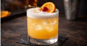 Classic whiskey sour cocktail with egg white foam, bourbon, lemon juice, and cherry orange garnish in a rocks glass