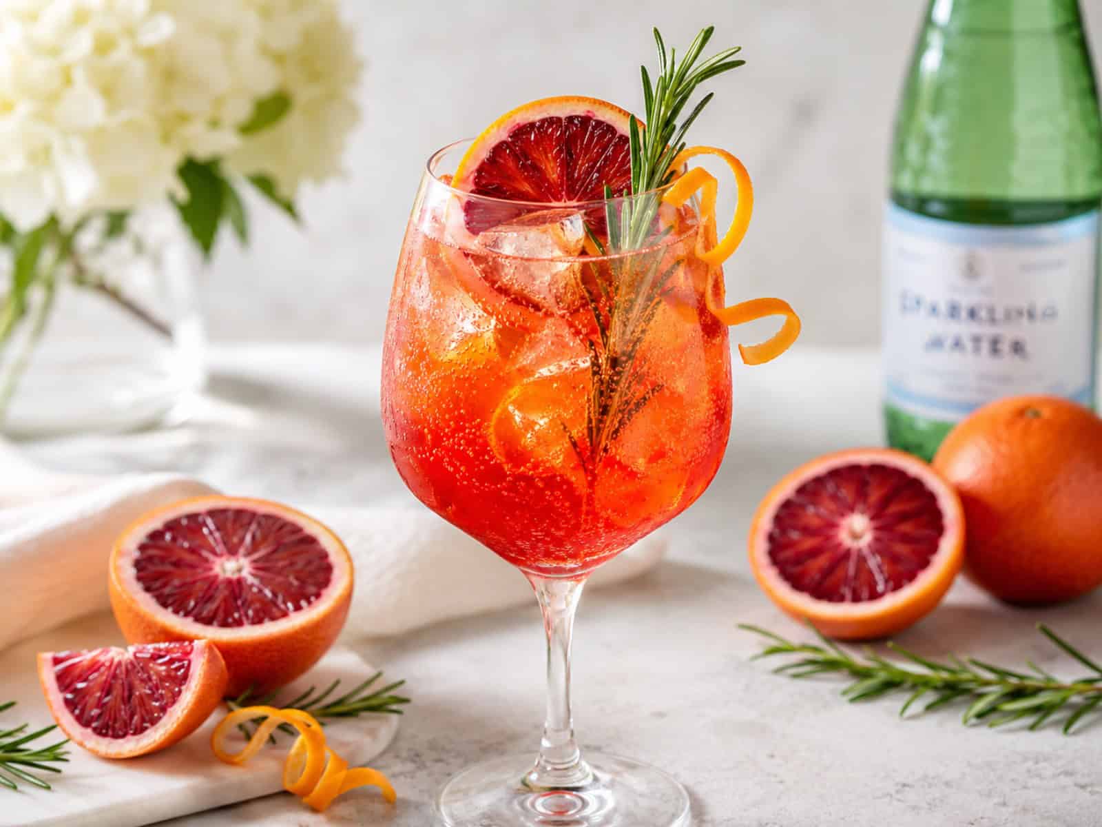 A blood orange spritz mocktail in elegant glassware with blood orange, rosemary, bubbles, citrus garnish, and ice.