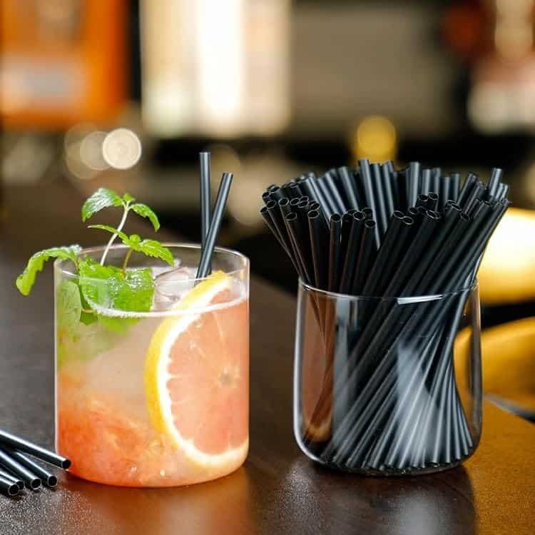 Short black disposable cocktail straws beside a citrus cocktail