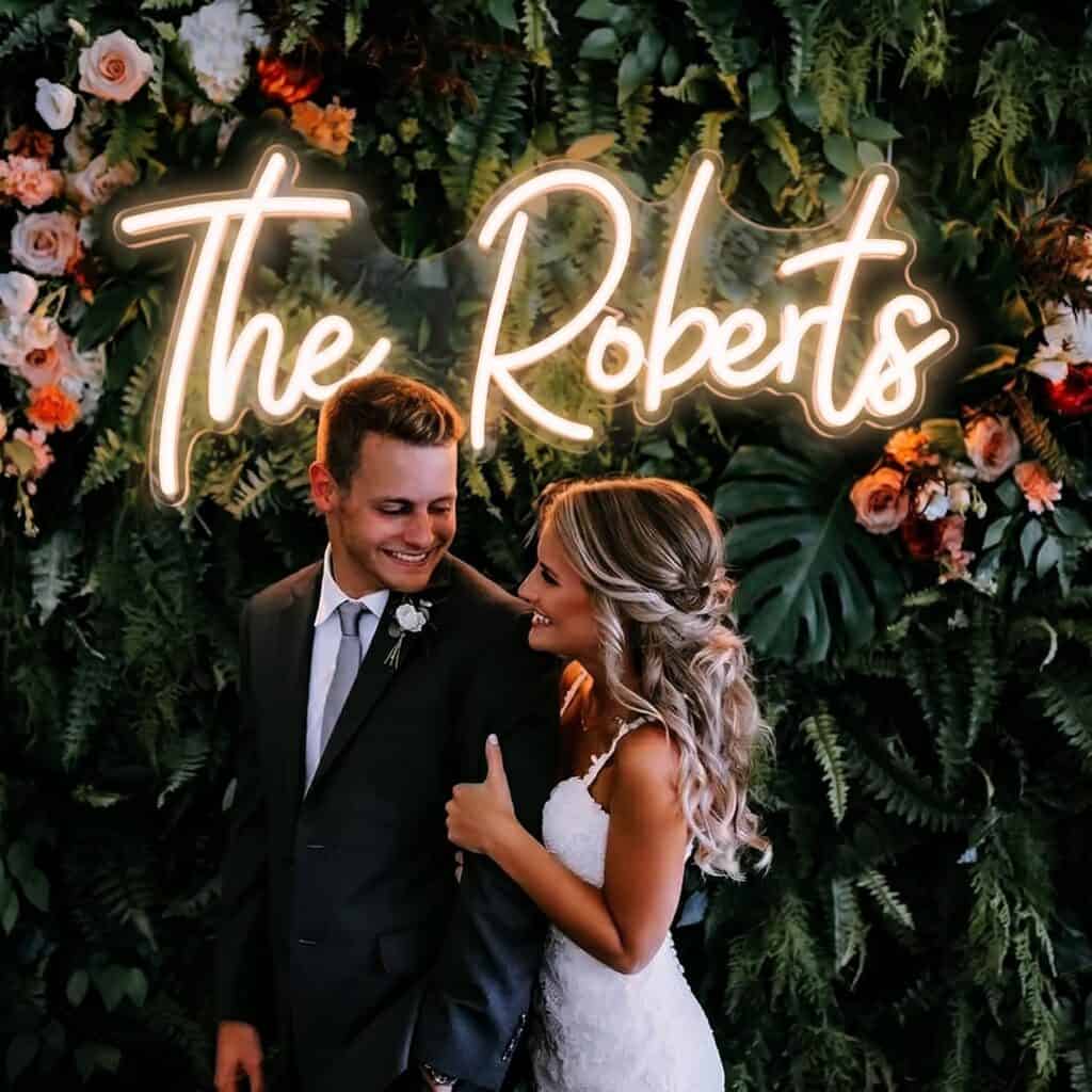 Custom illuminated wedding neon name sign displayed against a floral greenery wall